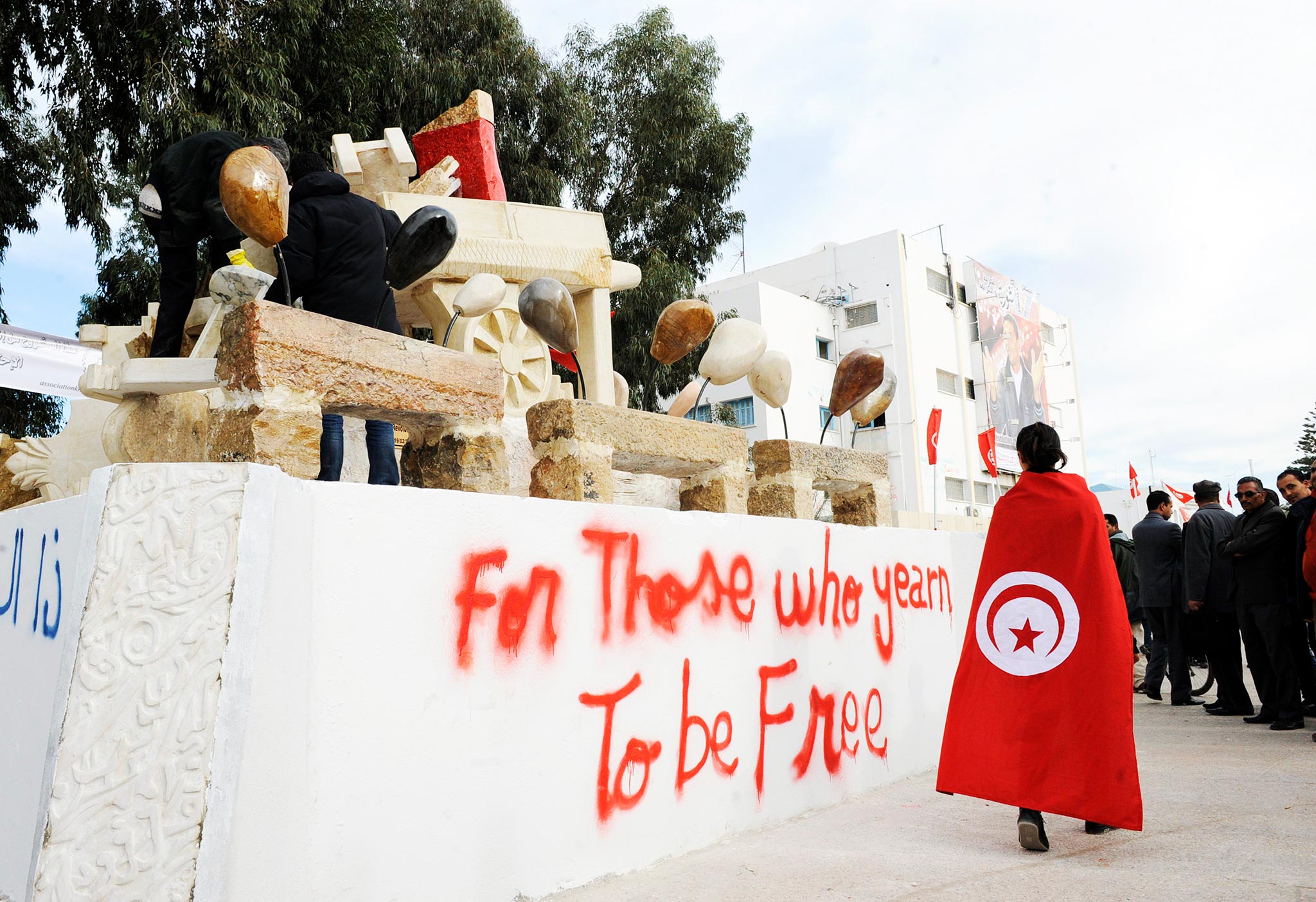 Kuvassa Tunisian lippuun kääriytynyt mies kulkee ohi patsaan, joka edustaa hedelmäkauppias Mohamed Bouazizia.
