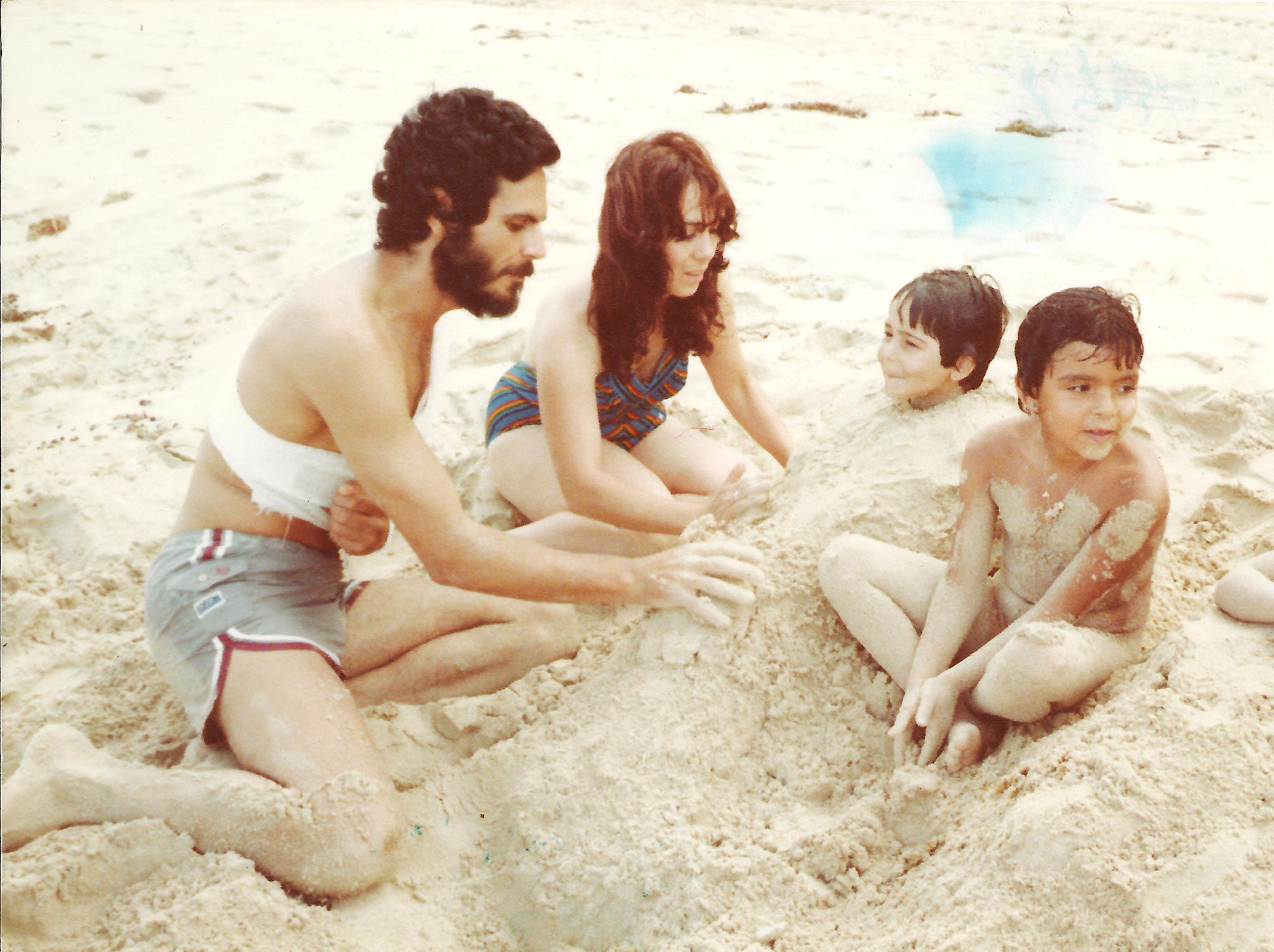 Kuvassa kaksi pikkulasta hiekkarannalla venhempiensa kanssa.