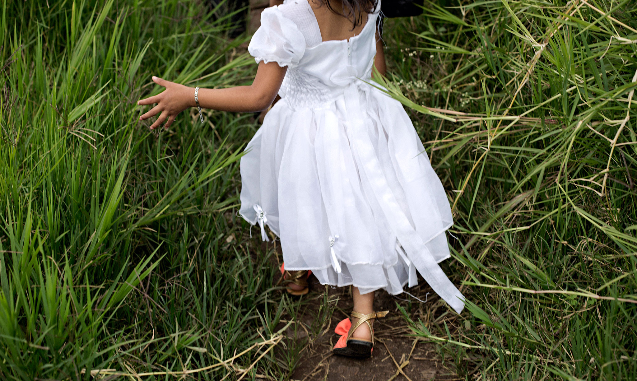 Tyttö valkoisessa mekossa juoksee korkeassa ruohosssa