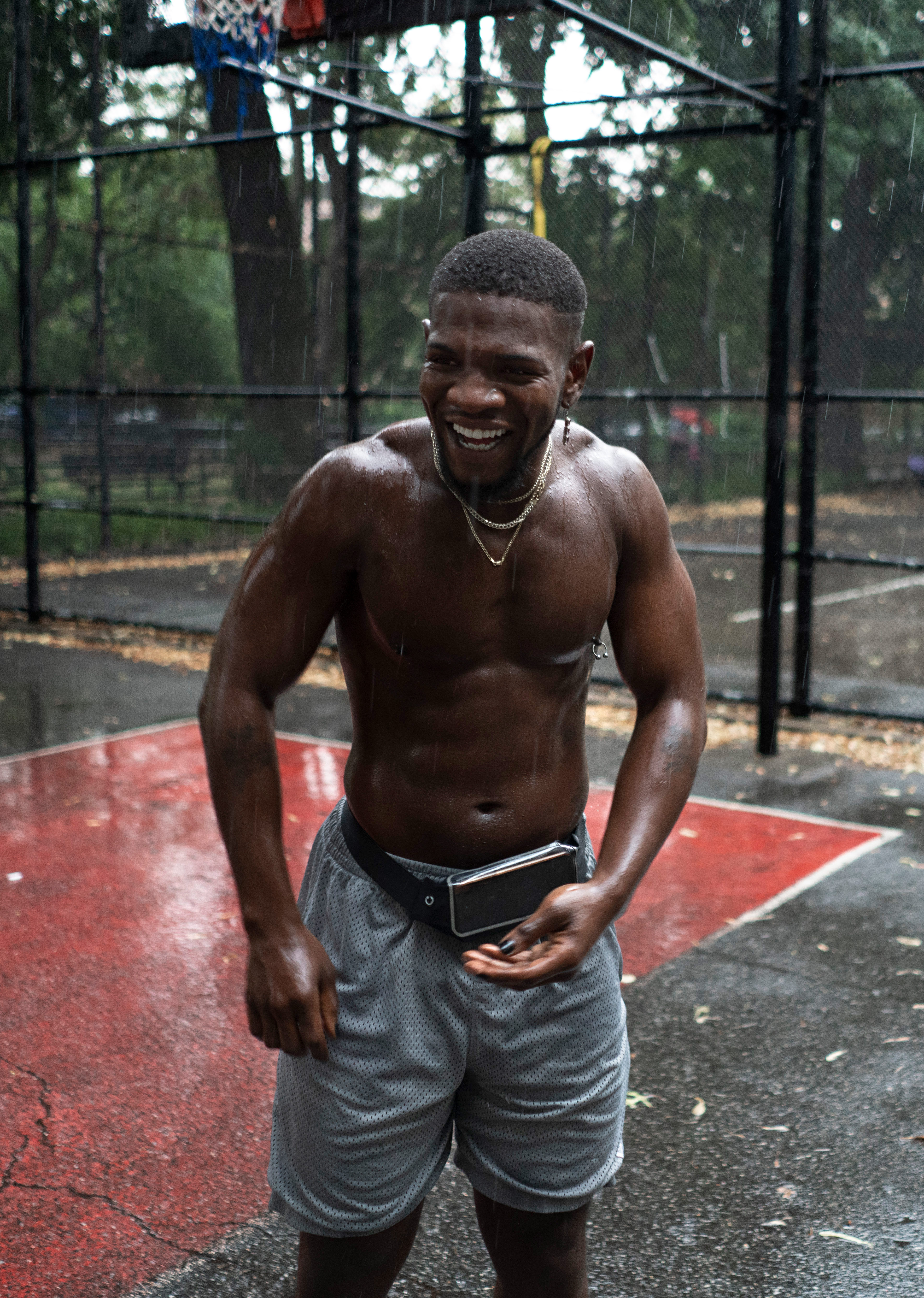 Mies nauraa sateessa paidattomana koripallokentällä.