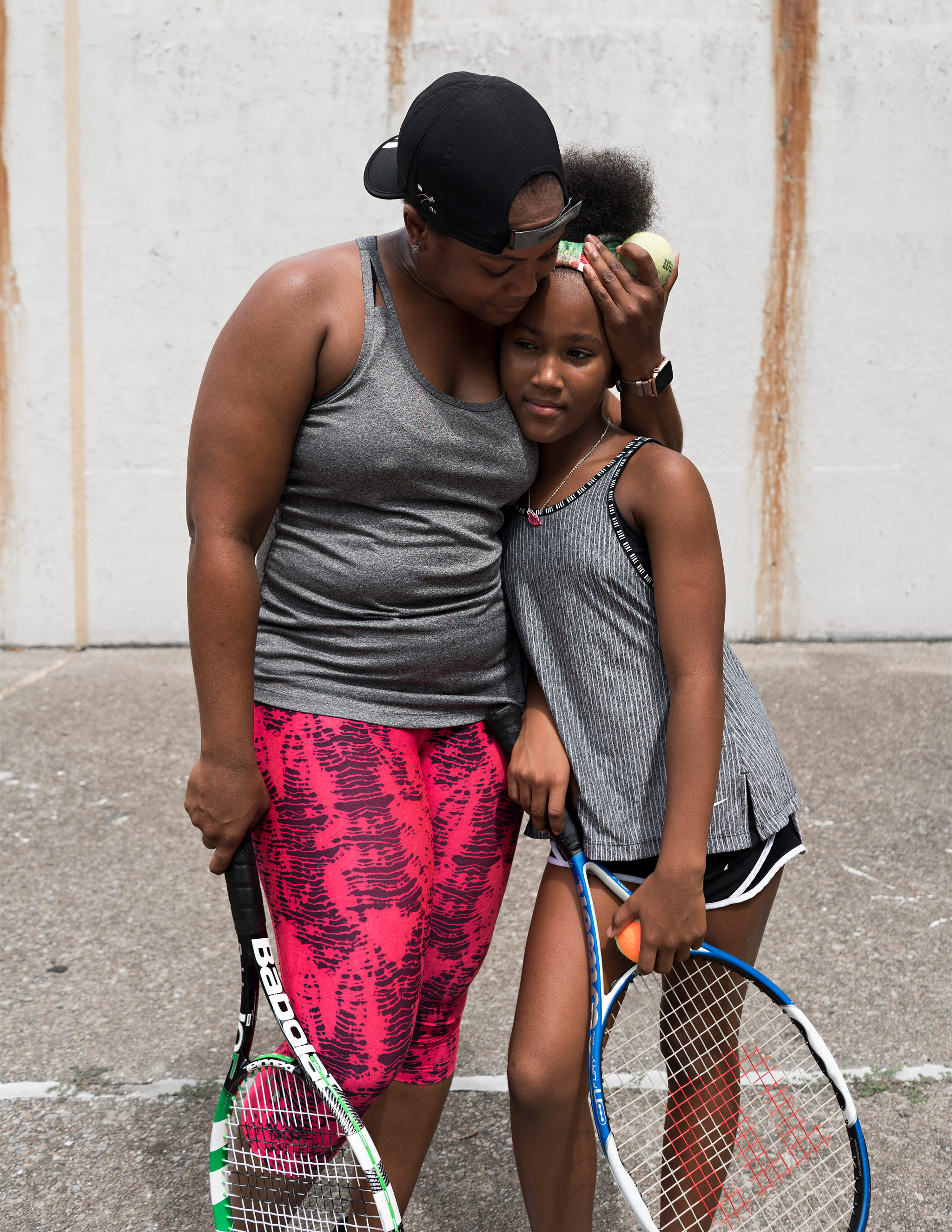 Äiti ja tytär tennismailat kädessään asvalttisella kentällä.