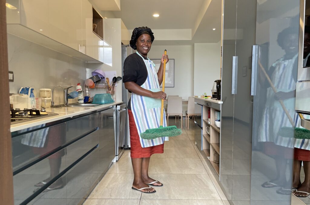  Nainen seisoo kiiltävässä keittiössä harja kädessään.
