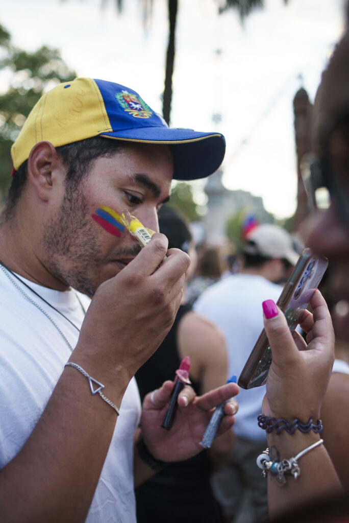 Mies maalaa Venezuelan lippua kasvoilleen mielenosoituksessa.