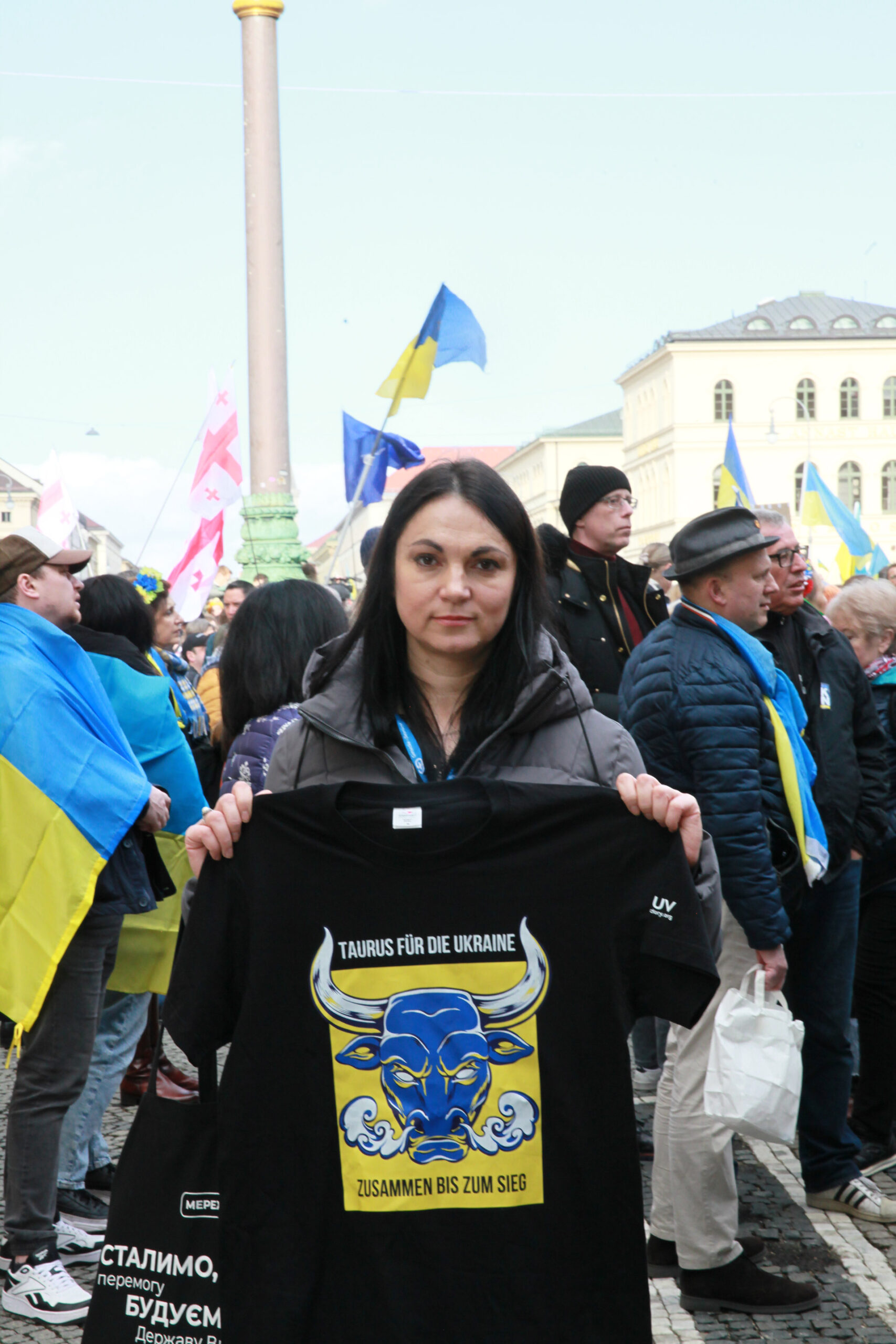 Hanna Hopko kädessään t-paita, jossa on Ukrainan lipun värit, taustalla ihmisiä ja Ukrainan lippuja.