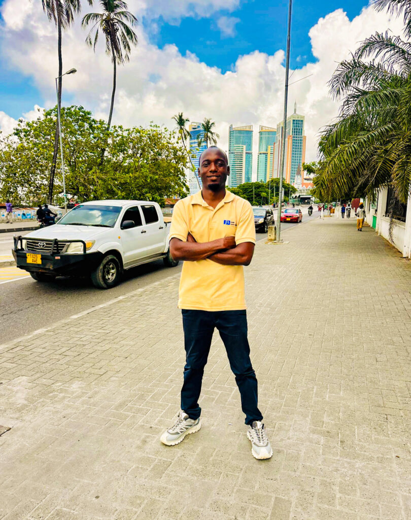 Frederick Ngowi seisoo kadulla, taustalla auto ja puita.